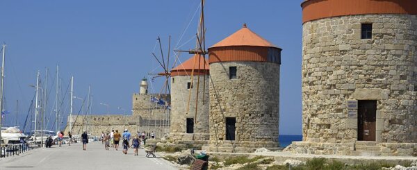 Drei historische Steinkornmühlen mit roten Dächern am Hafen von Rhodos, Menschen spazieren auf dem Kai