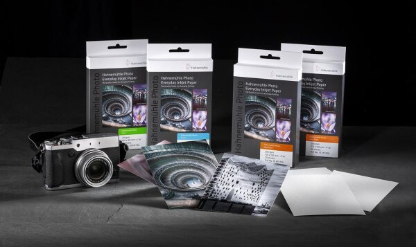 Vier Packungen Hahnemühle Everyday Inkjet Photo Paper 10x15 cm, 200 g/m², mit je 50 Blatt, daneben eine analoge Kamera und mehrere gedruckte Fotos