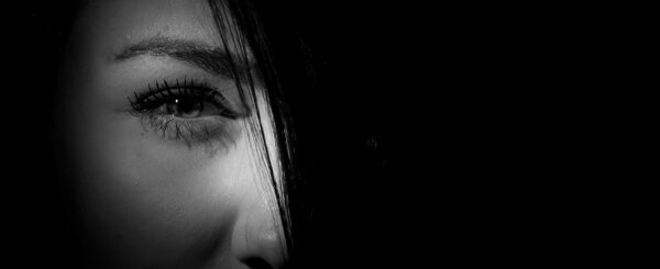 Schwarz-weiß-Porträt einer Frau mit Haaren vor einem Auge